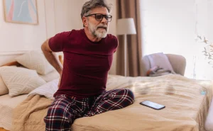 Man experiencing back pain while sitting on a bed.