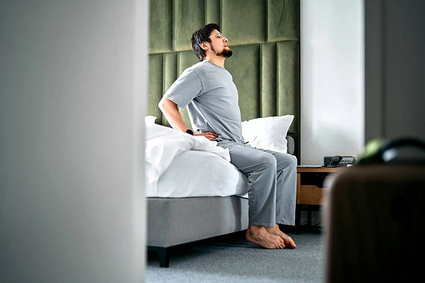 Man sitting on a bed with back pain while adjusting his posture for sciatica relief