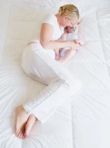 Mother and baby resting together on a bed for postpartum recovery.