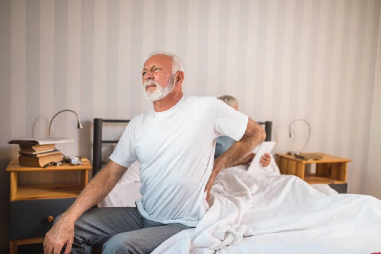 Older man sitting on bed with back pain, illustrating relief from swelling and improved circulation.