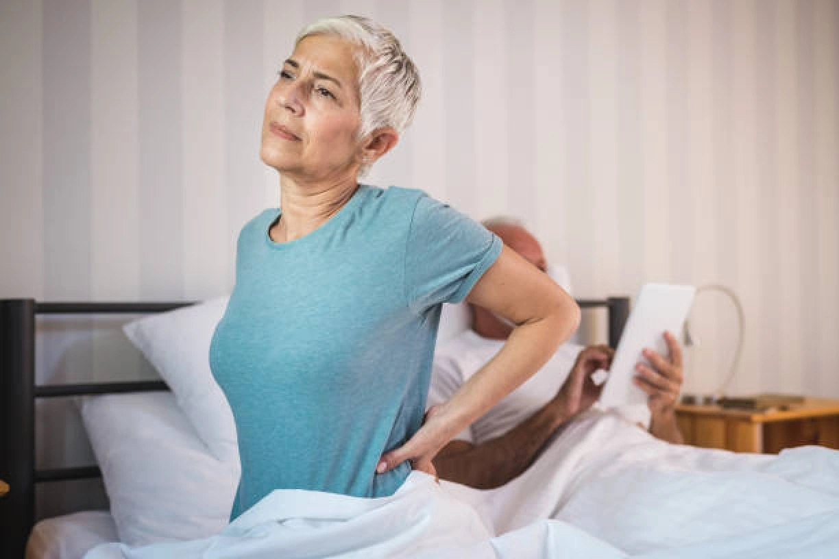 Older woman experiencing back pain while sitting on a bed, illustrating adjustable beds for back pain.