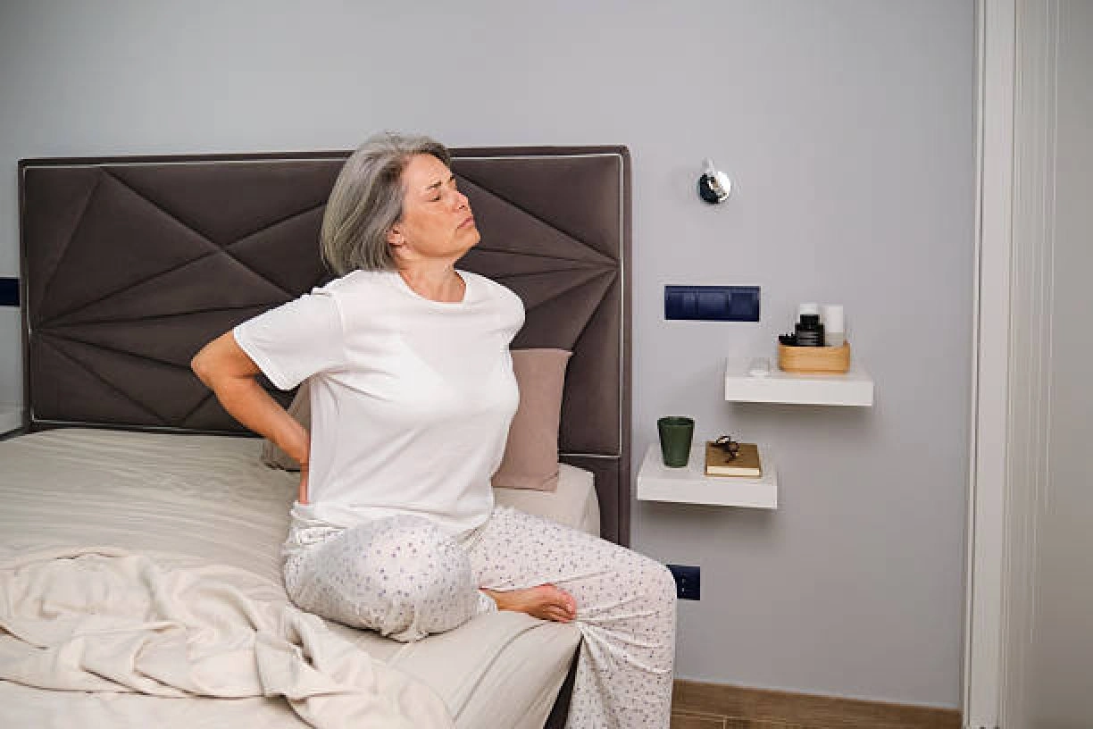Older woman experiencing back pain while sitting on a bed, illustrating smart adjustable beds for back pain.