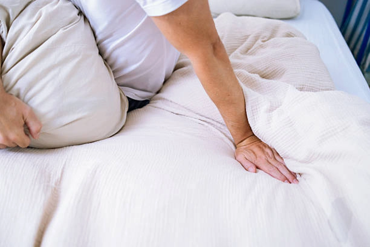 Person adjusting a bed for back pain relief with supportive pillows.