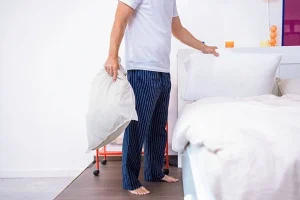 Person standing beside a bed with a pillow, illustrating adjustable bed positioning.