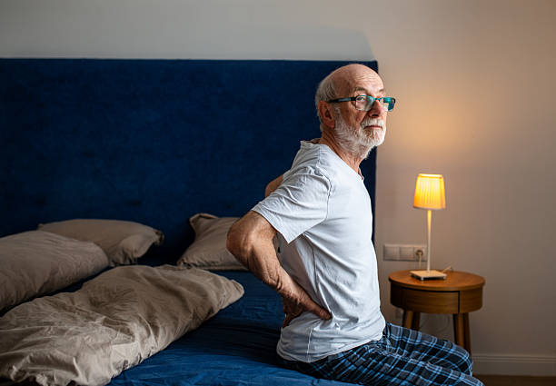 Senior man experiencing back pain while sitting on his bed