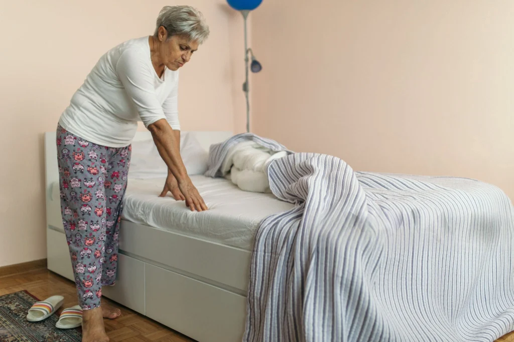Senior woman adjusting bedding to help prevent bed sores.