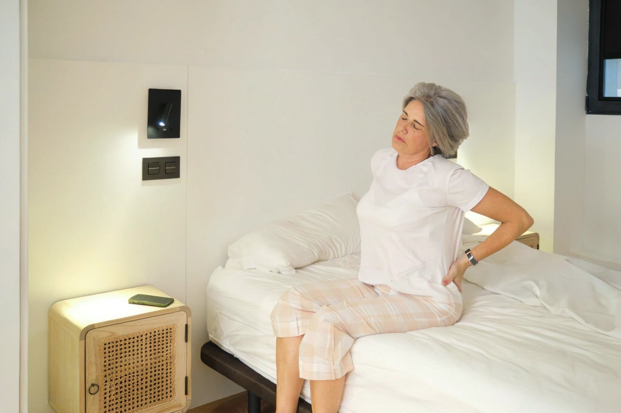 Woman with back pain sitting on bed after spine surgery.